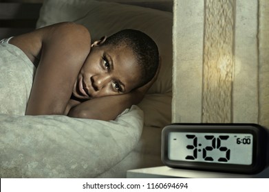 Lifestyle Portrait Of Young Sad And Depressed Black Afro American Woman Awake On Bed Sleepless Suffering Insomnia Sleeping Disorder And Anxiety Problem With Alarm Clock Late Night Hour