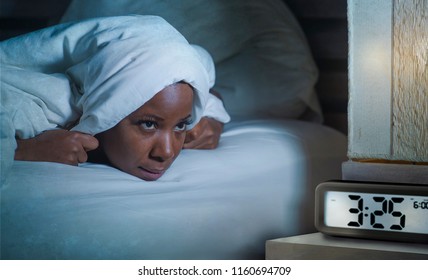 Lifestyle Portrait Of Young Sad And Depressed Black Afro American Woman Awake On Bed Sleepless Suffering Insomnia Sleeping Disorder And Anxiety Problem With Alarm Clock Late Night Hour