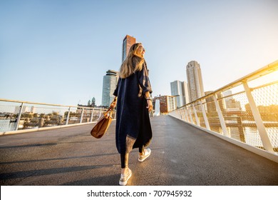 Lifestyle Portrait Of A Young Stylish Businesswoman Walking The Bridge During The Morning In Rotterdam