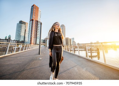 Lifestyle Portrait Of A Young Stylish Businesswoman Walking The Bridge During The Morning In Rotterdam