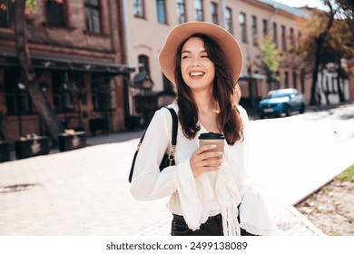 Lifestyle portrait of young stylish woman dressed in white blouse. Model walking with coffee cup in old town in sunny day. Beautiful smiling female in hat. Cheerful and happy. Takeaway coffee  - Powered by Shutterstock