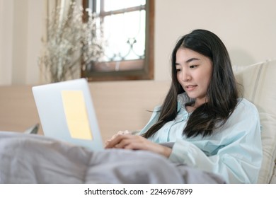 Lifestyle routine with internet technology concept. Young adult asian woman using laptop on bed for telemedicine mental health. People rest in bedroom activity.