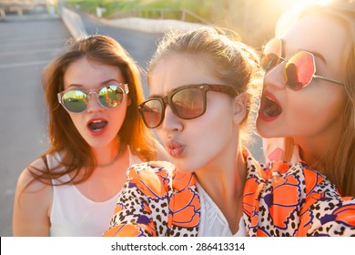 lifestyle self-portrait of tree best friends hipster girls wearing stylish bright outfits, denim shorts and glasses,going crazy and make funny faces,emotional people.Sunset background,urban city