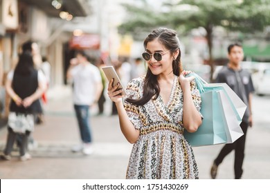 Lifestyle Shopping Concept, Young Happy Asian Woman With Mobile Phone And Paper Bag In Outdoor Shopping Street, Bangkok, Thailand