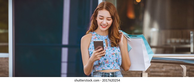 Lifestyle Shopping Concept, Young Happy Asian Woman Using Mobile Phone With Paper Bag In Shopping Mall, Bangkok, Thailand