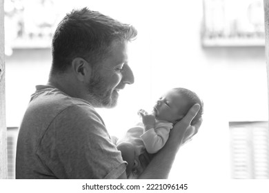 Lifestyle Shot In Black And White Of Young And Happy Man Holding Tenderly In His Arms Adorable Newborn Baby Girl  In Father And Daughter Love And Care Concept