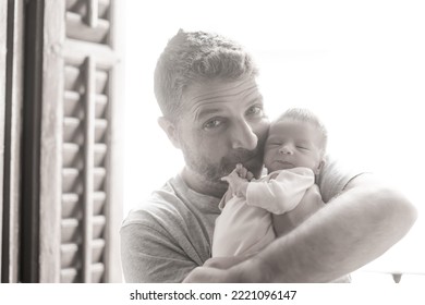 Lifestyle Shot In Black And White Of Young And Happy Man Holding Tenderly In His Arms Adorable Newborn Baby Girl  In Father And Daughter Love And Care Concept