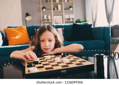 Lifestyle Shot Of Smart Kid Girl Playing Checkers At Home. Board Games For Kids Concept, Candid Series With Real People In Modern Interior