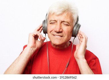 Lifestyle, Tehnology And Old People Concept: Handsome Old Man In Casual Wear And Headphones Is Listening To Music Over White Background