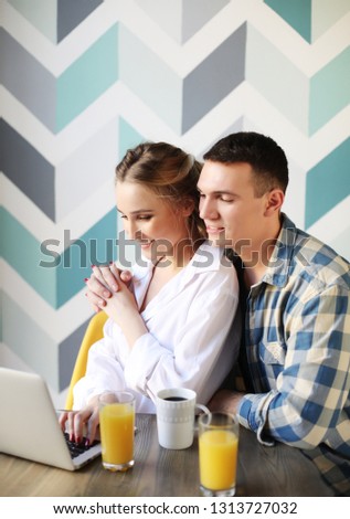 lifestyle, tehnology and people concept - Portrait of a laughing loving couple having breakfast while sitting at the table in a kitchen at home and looking at laptop computer