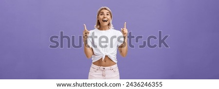 Lifestyle. Woman seeing miracle being impressed and delighted like child staring and pointing up with broad thrilled smile standing over purple background in summer trendy outfit being joyful and
