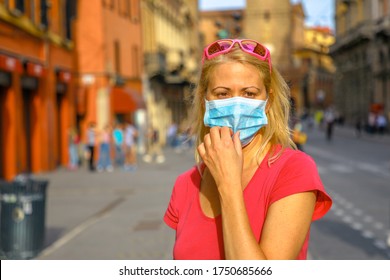 Lifestyle woman with surgical mask in Rizzoli road with Two Towers building at sunset. COVID-19 Coronavirus after quarantine with social distancing in Bologna city of Italy.