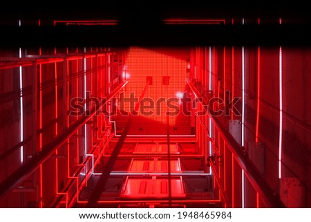 Lift shaft in a residential building. Elevator corridor in the building lit by red elumination. Futuristic elevator shaft is located in a high tower. Abstract, background. Bottom view