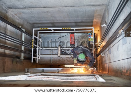 lift worker welding elevator fasteners in lift shaft