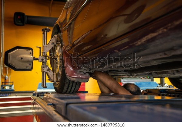 A lifted car repairing by the Asian mechanic.\
Lifted car in the garage being diagnostics by the professional\
mechanic to fix and balancing the tire. A lifted vehicle being\
maintenance in the garage