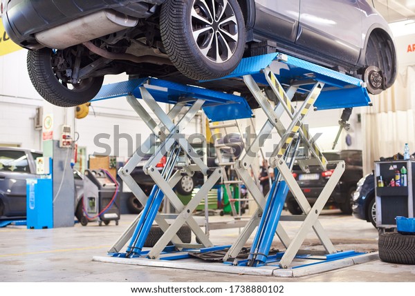 Lifted\
car without wheel waiting for repair in service station. Working\
area with automobile on high lift at vehicle repair shop. Concept\
of service center in process of car\
maintenance.