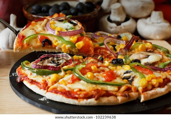 lifted Vegetarian\
pizza slice with a topping of Mushroom, Tomatoes, peppers, onions,\
sweetcorn and olives