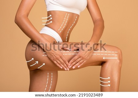 Lifting and anti-age concept. Young woman with massage lines and arrows on her body touching skin on leg, making heart sign gesture with hands, beige studio background