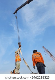 Lifting progress at construction site supervised by signalman or rigger. Ensuring safety and precision. 