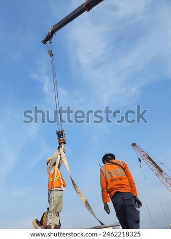 Lifting progress at construction site supervised by signalman or rigger. Ensuring safety and precision. 