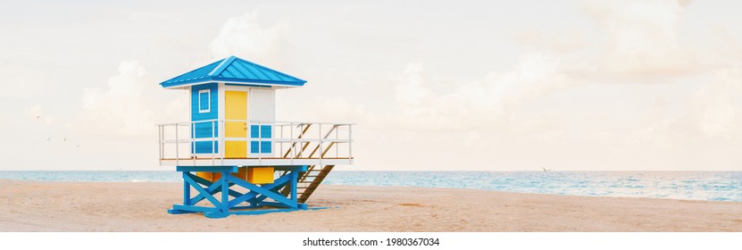 Light Airy Tropical Florida Landscape With Blue Yellow Lifeguard House. American Florida Nature Ocean View With Lifeguard Tower, Water, Sand And Sky. Empty Beach Outdoors. Web Banner Header.