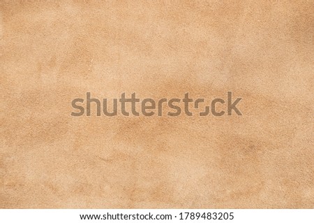 Light beige matte background of suede fabric, closeup. Velvet texture of seamless sand leather