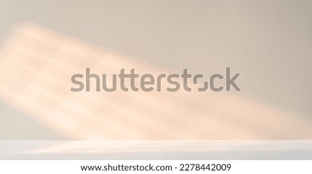 A light beige wall with sunlight beams and white table or floor for product presentation background.