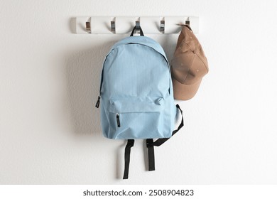 Light blue backpack and cap hanging on white wall