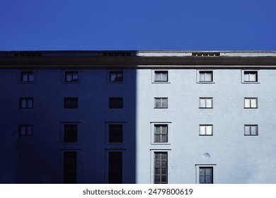 A light blue building in Europe,  minimalistic architecture. Blue sky on a sunny day. Windows reflecting the light from the sun, the game of shadows and light - Powered by Shutterstock