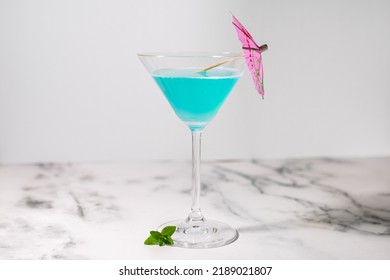 Light Blue Cocktail With Cocktail Umbrella On Marble Table And White Background