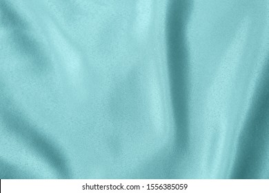 Light blue colored Background of soft draped fabric. Beautiful satin silk textured cloth for making clothes and curtains. Elegant textile texture.