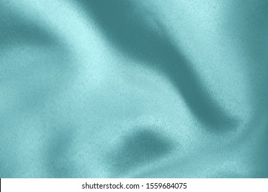 Light blue colored Background of soft draped fabric. Beautiful satin silk textured cloth for making clothes and curtains. Elegant textile texture.
