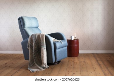 Light blue contemporary recliner armchair with plaid, painted old barrel serving as table for white mug and burning candle. Home interior. 