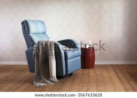 Light blue contemporary recliner armchair with plaid, painted old barrel serving as table for white mug and burning candle. Home interior. 
