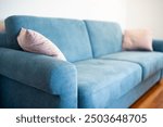 Light blue fabric sofa with cushions inside apartment room. Close up, side view, shallow depth of field, no people