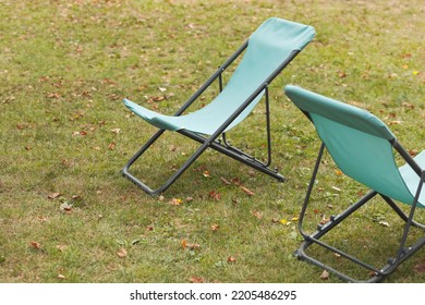 Light Blue Foldable Canvas Chairs Empty On Grass With Fallen Leaves, Close Up 