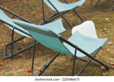 Light Blue Foldable Canvas Chairs Empty On Grass With Fallen Leaves, Close Up 