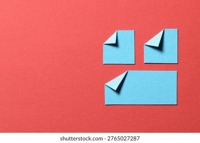 Light blue paper message notes or sheets with folded edge dog-ear earmark and copy space for text on red background, top view flat lay conceptual desk backdrop
