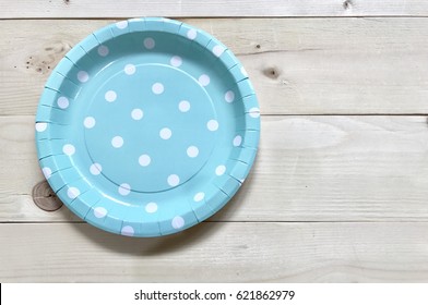 A light blue paper plate with white polka dots set on wooden background. The concept of party accessories. Focus some points.