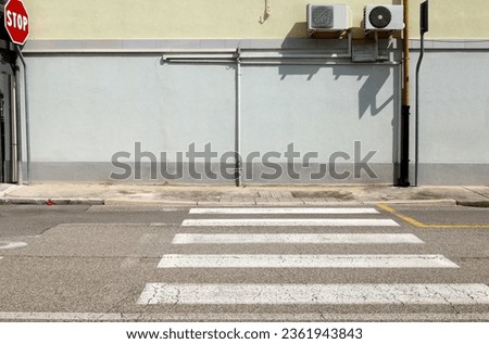 Light blue plaster wall with pipe of air conditioner unit in the middle. Concrete sidewalk and urban road with crosswalk in front. Urban background for copy space.