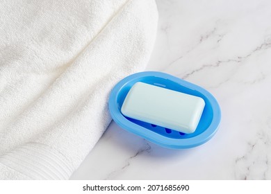 Light Blue Soap Bar On A Dish Near White Cotton Terry Towel Over Marble Surface. Washing Hands With Soap In The Morning And Before Going To Bed, Hygiene, Purity And Toiletries Concepts. Close-up.