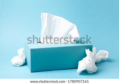 Light blue tissue box and crumpled tissues on blue background. Cold and flu concept. Minimal monochromatic composition.
