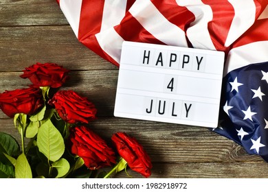 Light box with text HAPPY 4 JULY and flowers roses on a dark wooden background. Flat lay. Independence Day USA concept. Greeting card.