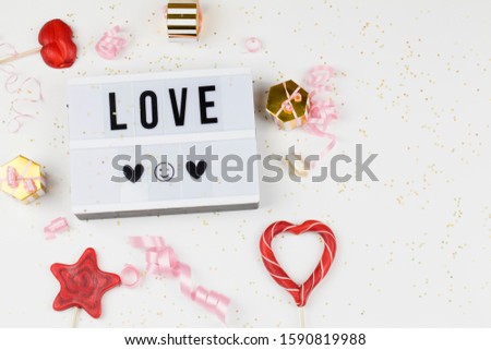 light box with text LOVE, decoration, gifts, red lollipops and ribbon. love confession, happy valentines day, greeting card, copy space for text concept. top view close up flat lay