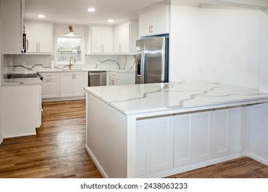 Leichte und helle, neu renovierte weiße Küche mit Quarzarbeitsplatten, weißen Schränken und goldener Hardware und rostfreien Geräten und einer großen Insel. – Stockfoto