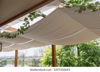 light brown fabric roof for sun protection. A hinged fabric roof, a summer patio, protection from the sun and heat, the interior of an outdoor cafe, white fabric on the ceiling.