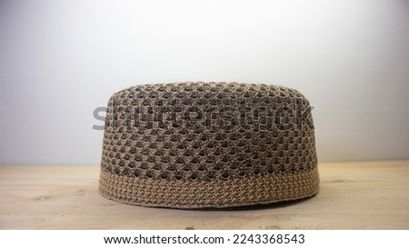 The light brown Islamic cap with a black combination with a knitted pattern is usually worn by Muslim men with a wooden background