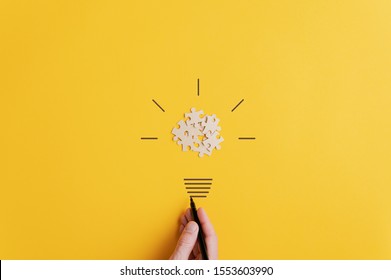 Light bulb of blank puzzle pieces as the bulb and hand drawn neck and rays over yellow background in a conceptual image of vision and idea.