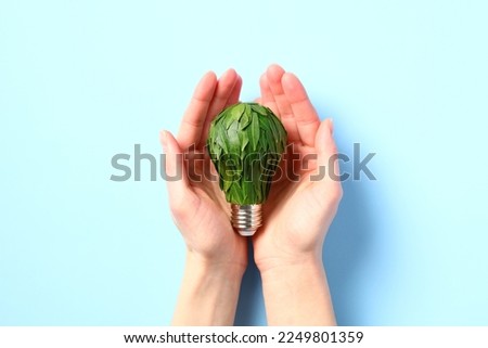 Light bulb in a female hand, adorned with plant leaves. Green energy and environmental protection concept.
