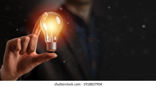 Light bulb in hand of man wearing suit in black background. New idea or inspiration concept.